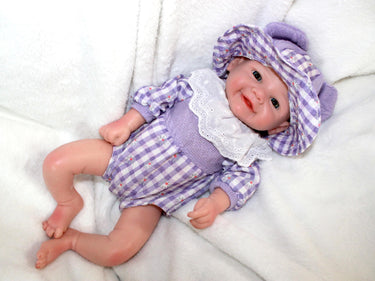 A baby doll dressed in a purple and white dress, featuring a sweet expression and soft, lifelike features.